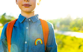 A girl in denim t-shirt with rainbow symbol wear backpack in summer park outdoor.