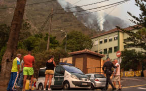 A civil guard talks with residents of La Orotava as a wildfire rages out of control through forested slopes on the Canary island of Tenerife, on August 19, 2023. More than 26,000 people may have been forced to flee a vast wildfire raging out of control in the Spanish holiday island of Tenerife, the emergency services said today. The huge blaze, which broke out late Tuesday in a mountainous northeastern area of the island, is the "most complex fire" to hit Spain's Atlantic Canary Islands in more than 40 years, the authorities say. (Photo by DESIREE MARTIN / AFP)