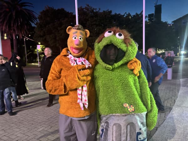 Two people stand outside - one in a bear costume and one in an Oscar the Grouch costume.