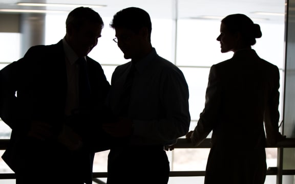 A man and two women in business dress stand on a balcony in an office.