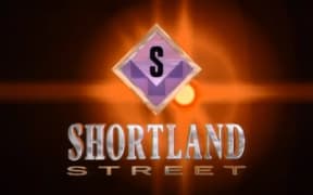 A screencap of the title sequence for Shortland Street from 1992. A glowing orange light on black background with the words "SHORTLAND STREET" in front of it, beneath a diamond with an S on it.