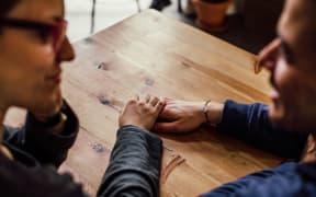 A couple looks at each other and hold hands over a wooden table