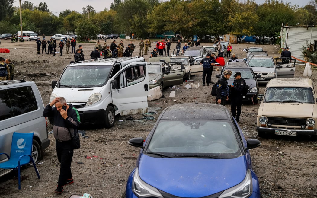 People walk between cars damaged by a missile strike on a road near Zaporizhzhia on September 30, 2022.
