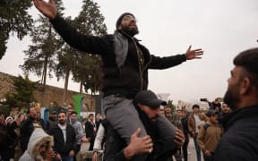 Celebrations in the city of Hama, where Syrians gather at Al-Assi Square to take commemorative photos and express their joy over the city's control. The square is filled with the sounds of celebratory gunfire and the distribution of sweets to mark the occasion.