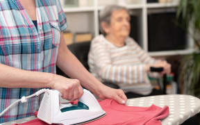 Home, helper ironing clothes for elderly woman.
