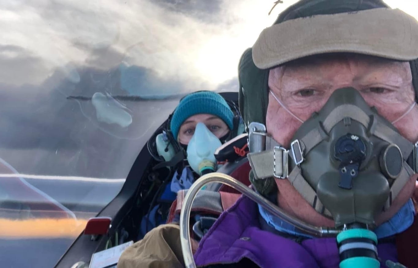 Two people, both wearing oxygen masks, in the cockpit of a glider.