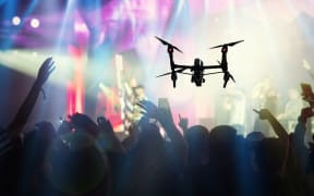 Closeup silhouette of Drone flying for taking video of Concert crowd and Music fanclub with show hand action which follow up the songer at the front of stage, musical and concert concept