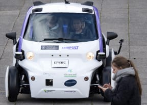 A woman uses a mobile phone as she walks in front of an autonomous self-driving vehicle, as it is tested in a pedestrianised zone, during a media event in Milton Keynes, north of London this month.