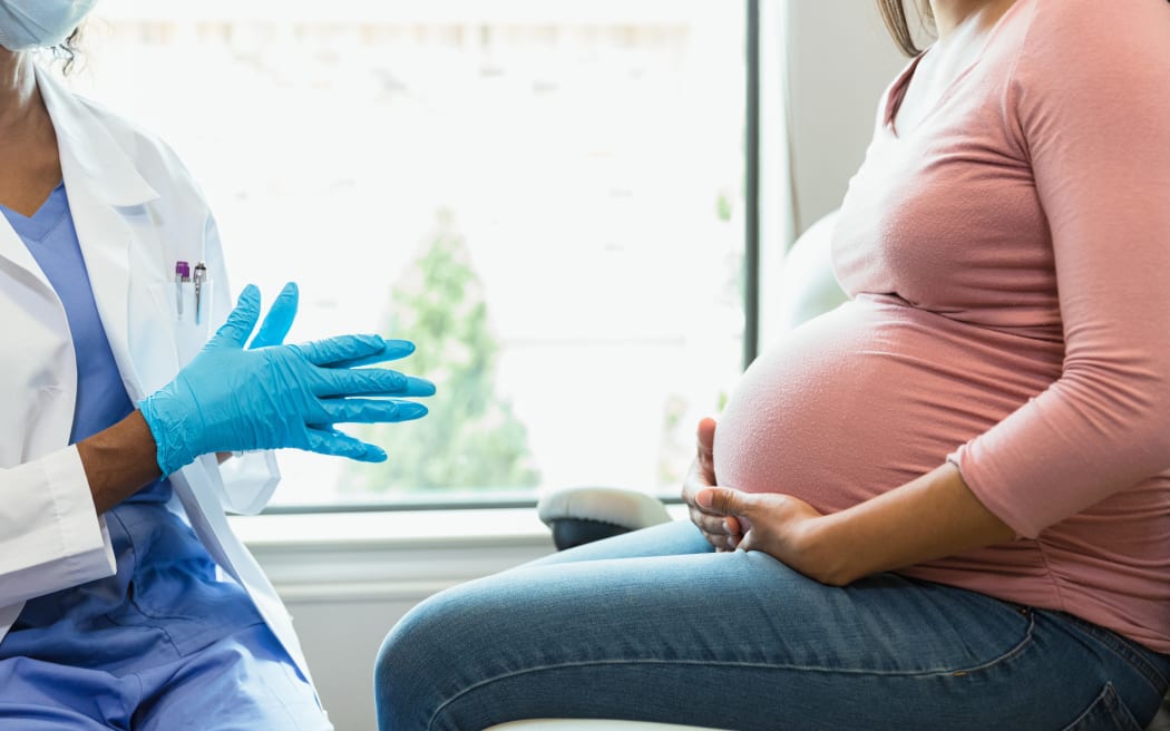 An unrecognizable female doctor wears protective mask and gloves as she prepares to examine an unrecognizable pregnant woman.