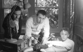 Bressa Creeting Cake are three young men huddled around a desk on which sits a strange-looking machine.