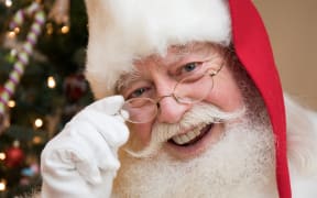 A close up portrait of Santa with a Christmas tree in the background.
