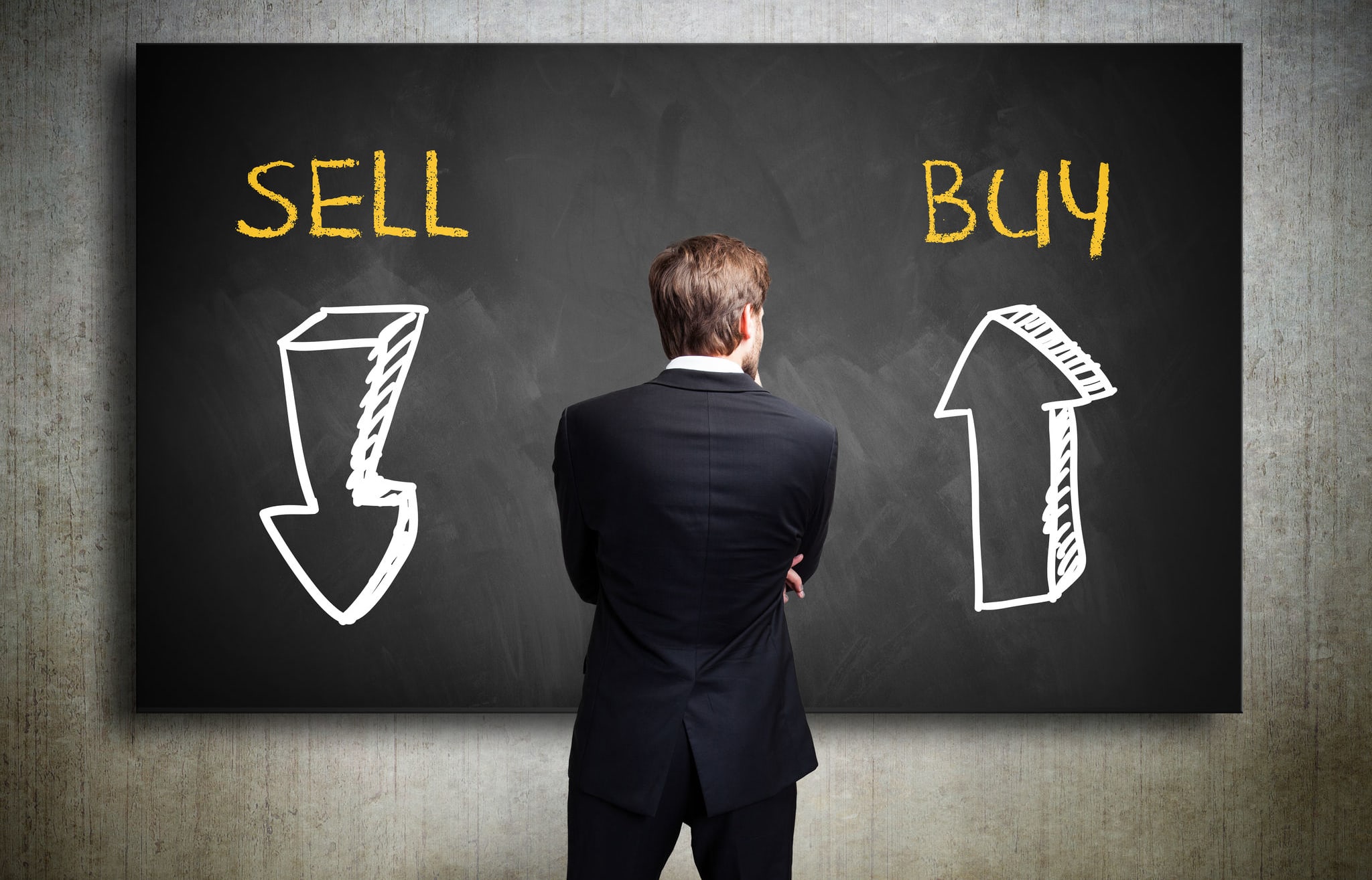 Businessman standing in front of a blackboard trying to decide whether to buy or to sell