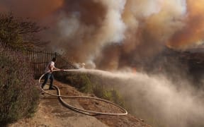 A resident attempts to protect his property from the flames closing in on homes threatened by the wind-driven Palisades Fire in Pacific Palisades, California, January 7, 2025. - A fast-moving brushfire in a Los Angeles suburb burned buildings and sparked evacuations Tuesday as "life threatening" winds whipped the region. More than 200 acres (80 hectares) was burning in Pacific Palisades, a upscale spot with multi-million dollar homes in the Santa Monica Mountains, shuttering a key highway and blanketing the area with thick smoke. (Photo by David Swanson / AFP)