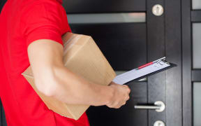 Delivery guy waiting at front door with a parcel.