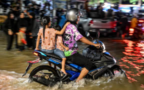 A man rides his motorbike through a flooded street after a heavy downpour in Kota Bharu, in Malaysia's Kelantan state, on November 29, 2024. - Flooding in northern Malaysia and southern Thailand has killed at least eight people and forced tens of thousands from their homes, officials in both countries said on November 29. (Photo by Mohd RASFAN / AFP)