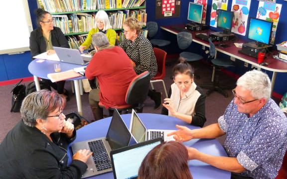 Eight principals sit at 2 round children's tables in a class room.