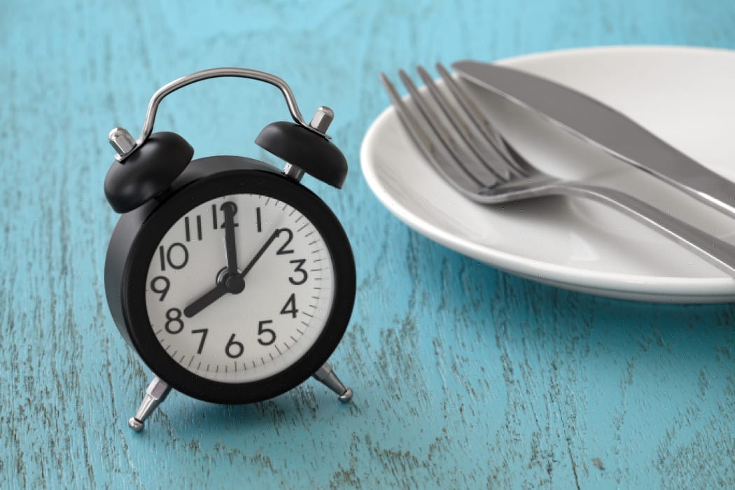 Clock with fork and knife on white plate, intermittent fasting, meal plan, weight loss concept