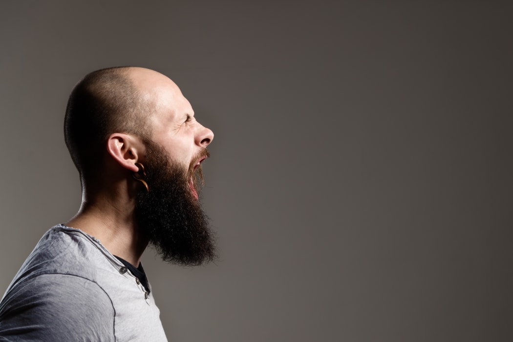 Side view portrait of screaming bearded man - gray background