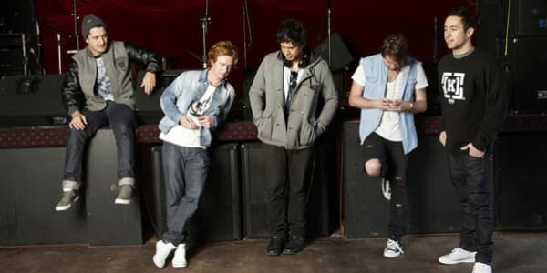 Six60 are five young men leaning against a stage, none looking at the camera.