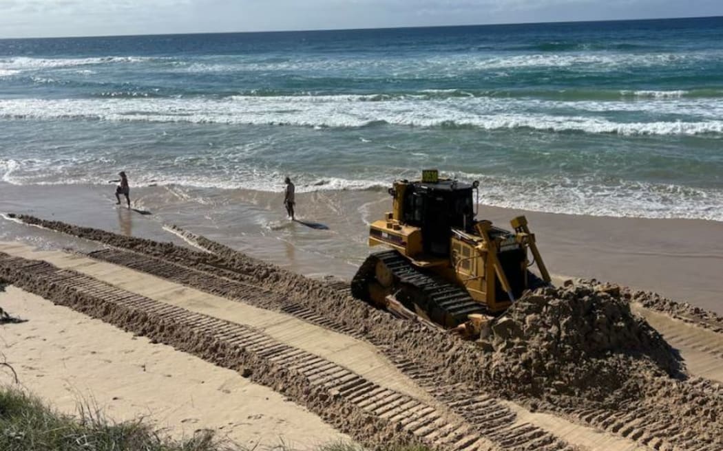 A bulldozer shifting sand on Surfers Paradise Beach at low tide.