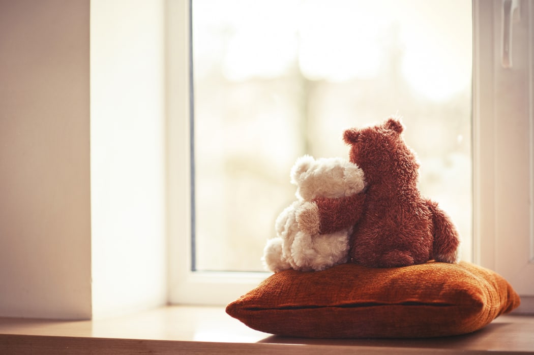 Two embracing teddy bears looking through the window sitting on window-sill.