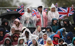 Members of the public cover themselves against the rain as they wait for the return of Britain's King Charles III and Britain's Camilla, Queen Consort outside Buckingham Palace, in central London, on May 6, 2023 ahead of their coronations. - The set-piece coronation is the first in Britain in 70 years, and only the second in history to be televised. Charles will be the 40th reigning monarch to be crowned at the central London church since King William I in 1066. (Photo by Marco BERTORELLO / AFP)