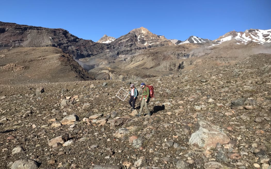 Two woman walk across a rocky high altitude landscape beneath a bluebird sky.