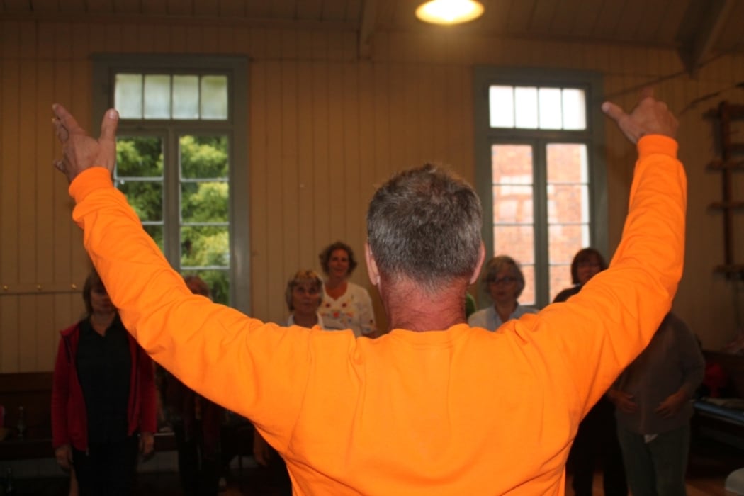 A photo looking over the shoulder of choirmaster Bert van Dijk as he leads the singers.