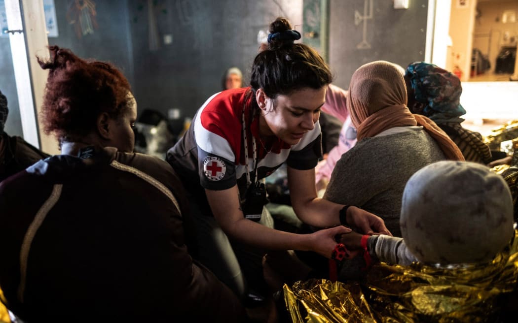 This photo taken on March 13, 2024 and handout on March 14, 2024 by international humanitarian organization SOS Mediterranee, shows a Monaco Red Cross volunteer (C) tending to a migrant child aboard the Ocean Viking rescue vessel, following a rescuing operation of migrants in the Libyan search and rescue region in international waters. The Ocean Viking migrant rescue vessel chartered by SOS Mediterranee rescued 25 people off the coast of Libya on March 13, 2024, who had been in "an inflatable boat adrift" for "around a week", the NGO said in a press release. "Those rescued report that many people have died and are now missing", said SOS Mediterranee. (Photo by Johanna de TESSIERES / SOS MEDITERRANEE / AFP) / RESTRICTED TO EDITORIAL USE - MANDATORY CREDIT "AFP PHOTO / HO / JOHANNA de TESSIERES / SOS MEDITERRANEE   " - NO MARKETING NO ADVERTISING CAMPAIGNS - DISTRIBUTED AS A SERVICE TO CLIENTS