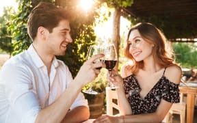 Picture of young loving couple sitting in cafe by dating outdors in park holding glasses of wine drinking.