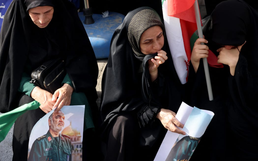 Women mourners holding posters of Iranian Islamic Revolutionary Guard Corps (IRGC) commander Hossein Salami sit on the edge of the pavement watching the funeral of the Iranian Revolutionary Guards commander and other military commanders killed in Israeli strikes on Iran, during their funeral procession at Enghelab (Revolution) Square in the capital Tehran on June 28, 2025. Iran began a state funeral service on June 28, for around 60 people, including its military commanders, killed in its war with Israel, after Tehran's top diplomat condemned the US' President's comments on Iran's supreme leader  as "unacceptable". (Photo by ATTA KENARE / AFP)