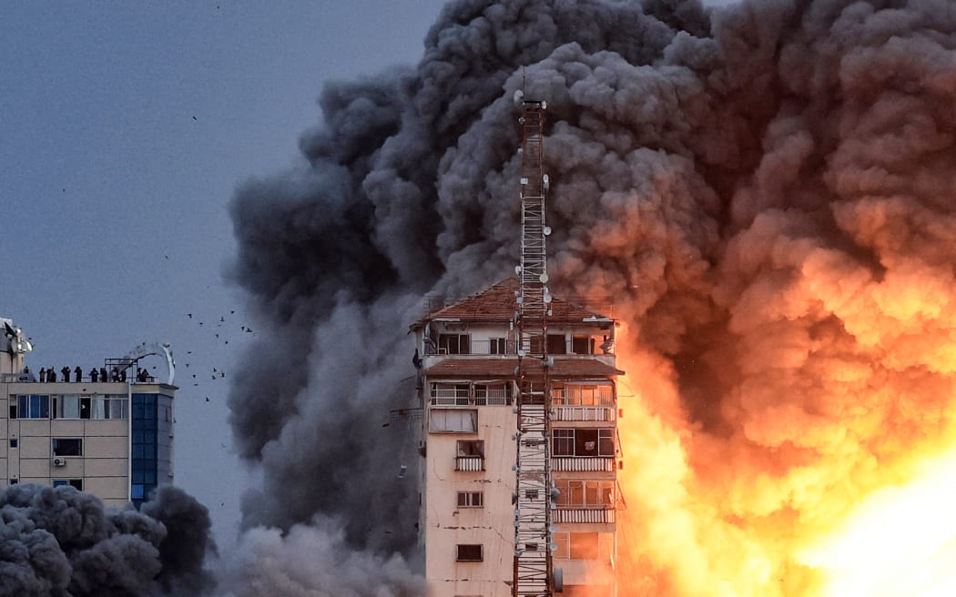 People standing on a rooftop watch as a ball of fire and smoke rises above a building in Gaza City on October 7, 2023 during an Israeli air strike. At least 70 people were reported killed in Israel, while Gaza authorities released a death toll of 198 in the bloodiest escalation in the wider conflict since May 2021, with hundreds more wounded on both sides. (Photo by MAHMUD HAMS / AFP)