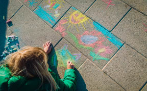 Child drawing outside on footpath with chalk.