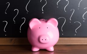 A file photo shows a piggy bank in front of a blackboard with question marks.