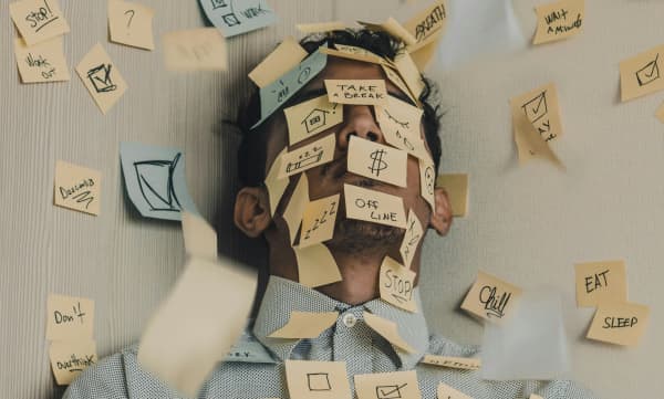 A man in a corner with post-it notes all over his face and the wall.