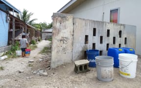 A young Majuro child carries fresh water in buckets to his house.