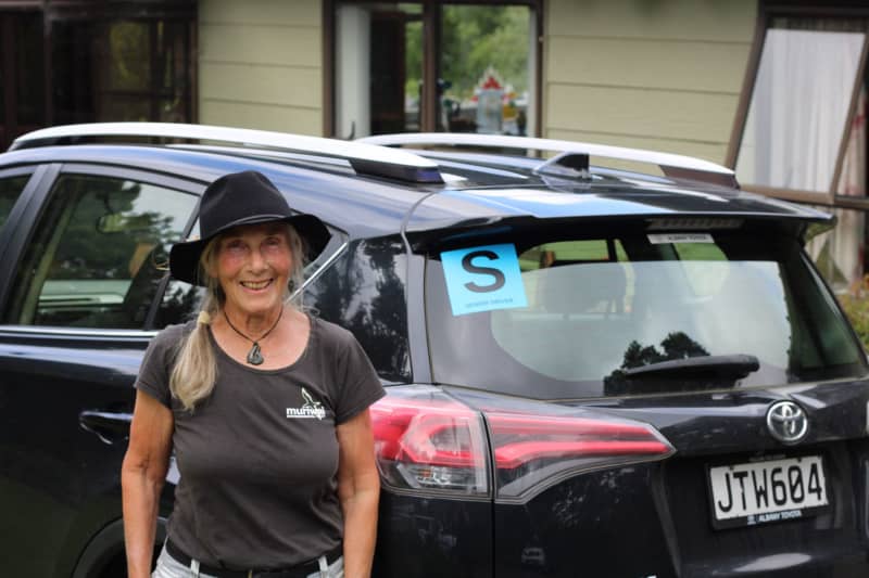 A woman standing near a car with the S sticker on the rear windshield.