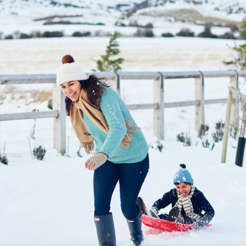 Nadia Lim laughs as she drags her son on a sled through the snow.