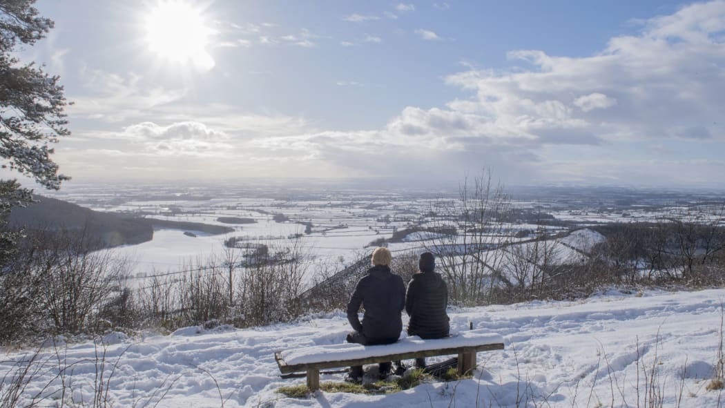 A couple sit on a bench overlooking snow-covered fields in North Yorkshire.
