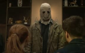A man in a spooky mask faces a young white heterosexual couple