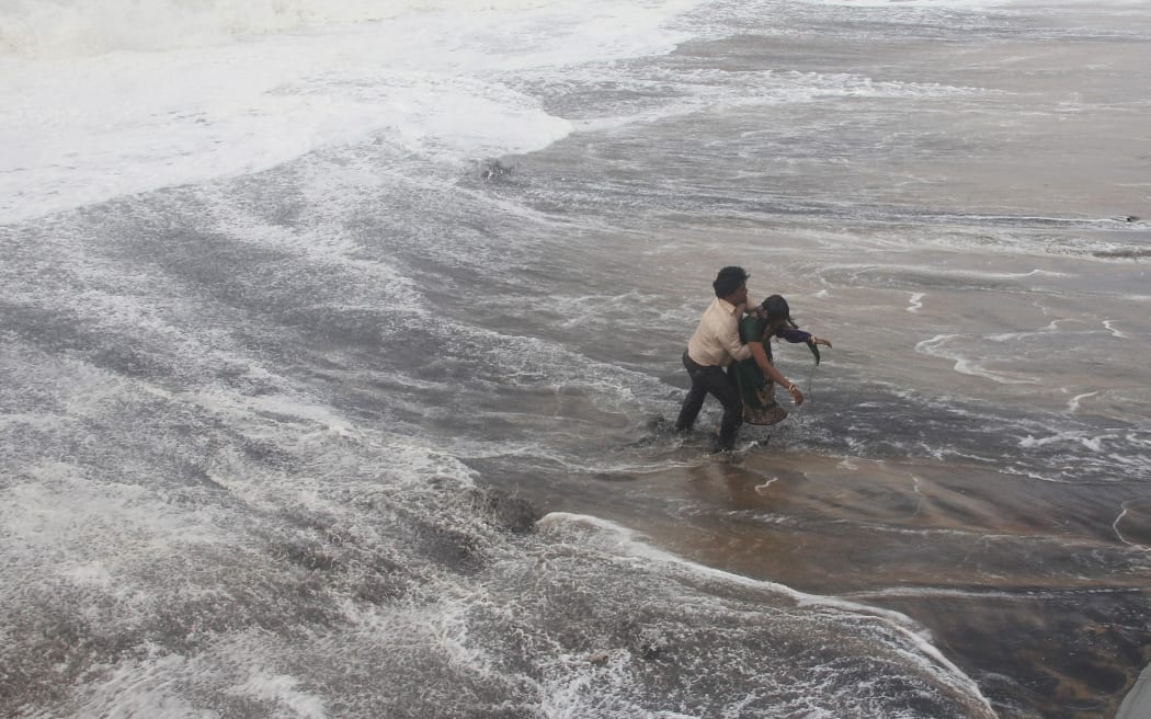 A man carries his wife to a safer ground after a wave hits a beach in Gopalpur in Ganjam district in the eastern Indian state of Odisha.