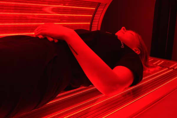 A woman lying down inside a red light therapy machine.