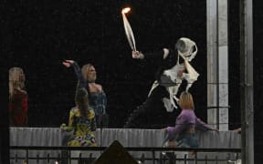 A torchbearer moves past models on a catwalk erected along the Passerelle Debilly bridge along the Seine river during the opening ceremony of the Paris 2024 Olympic Games in Paris on July 26, 2024. (Photo by Mauro PIMENTEL / AFP)