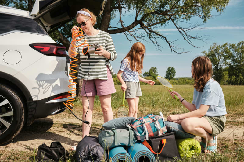 A family unpack their car with road trip items including bags and tennis rackets.