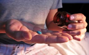 A young man in pajamas in bed about to take a blue pill.