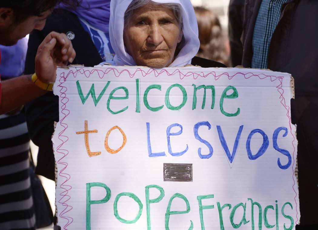 A woman holds a placard welcoming the Pope to the Moria refugee camp