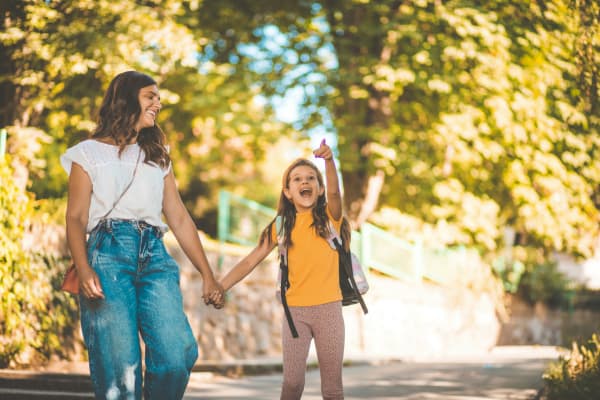 Woman holds young girls hand as they walk and she points at something in surprise.