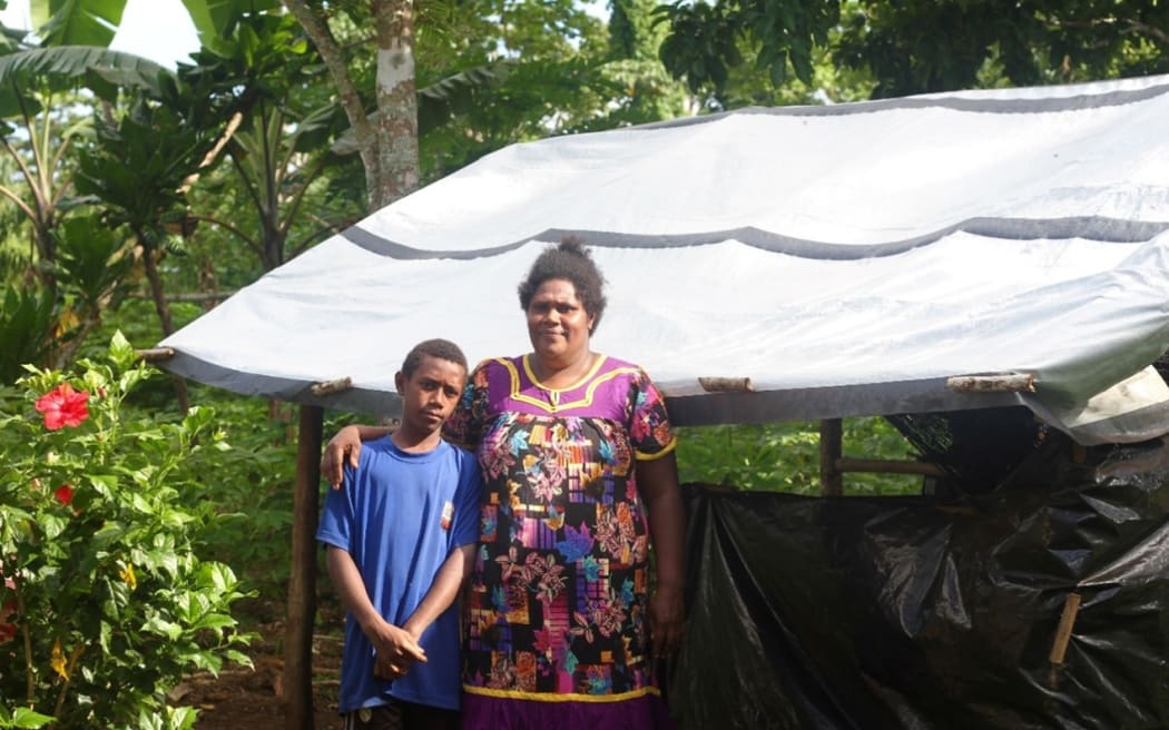 Noa, 11, and his mother Emele, 39 pictured in front of the tarp they are using for shelter one year on from the twin cycles that damaged their home.