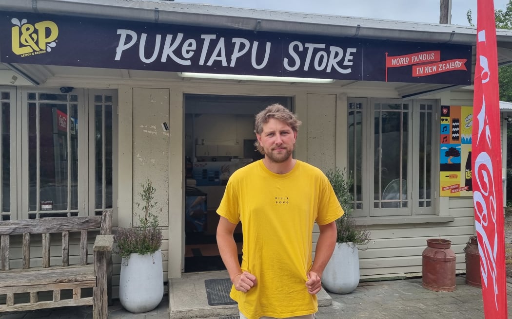 Puketapu Store owner Jaycen Maxwell stands outside the shop. He wears a yellow t-shirt.