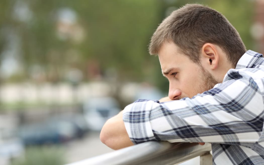 Side view portrait of a sad single man looking down from a balcony of a house  with an urban background